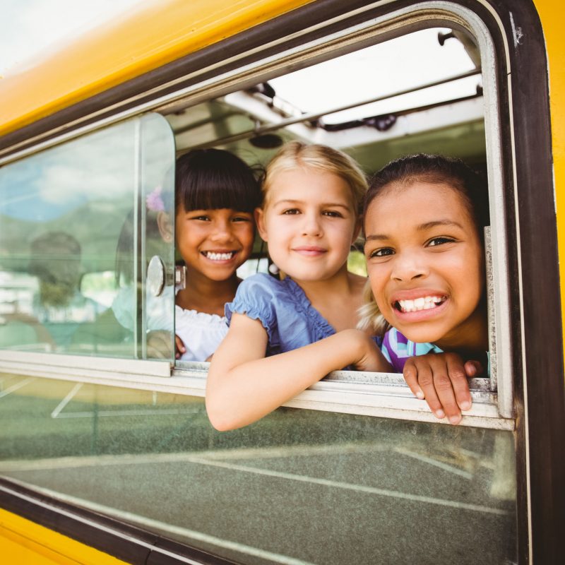 Cute pupils smiling at camera in the school bus outside the elementary school