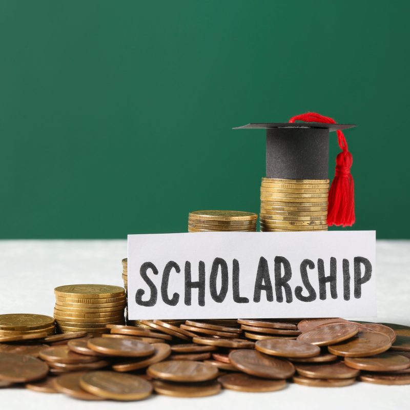 Paper with word Scholarship, graduation cap and coins on white table